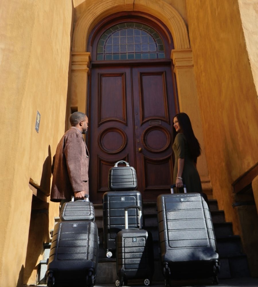 Lifestyle image of the Milan luggage set placed outside a hotel with a couple nearby, emphasizing its refined style, cohesive design, and premium presence for modern travelers