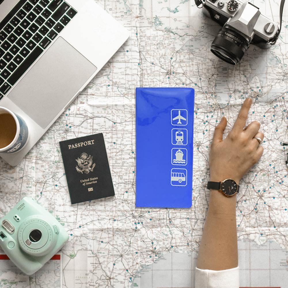 Lifestyle image of the Blue Passport Documents Cover placed on a table with a map, camera, coffee, laptop, and passport, with a hand pointing to a travel location—evoking a sense of journey and adventure
